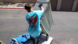 A mover from Rising Phoenix Movers LLC pushing a large, wrapped item on a dolly up a truck ramp in Phoenix, AZ.