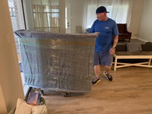 A mover from Reynolds Moving in Baton Rouge, LA, pushing a large, wrapped piece of furniture on a dolly