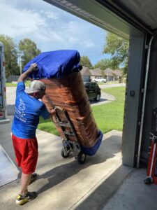 A mover from Reynolds Moving in Baton Rouge, LA, pushing a large, wrapped item on a dolly out of a garage towards a moving truck