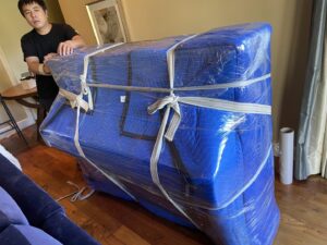 A mover pushing a large, wrapped piano on a dolly inside a home for IMoving Professional Moving System Inc. in San Francisco, CA