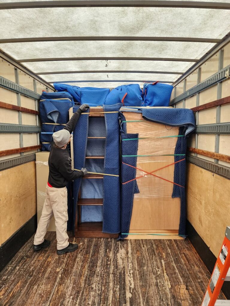 A professional mover from Joy Haul Professional Movers carefully securing wrapped furniture inside a moving truck in Columbia City, IN.