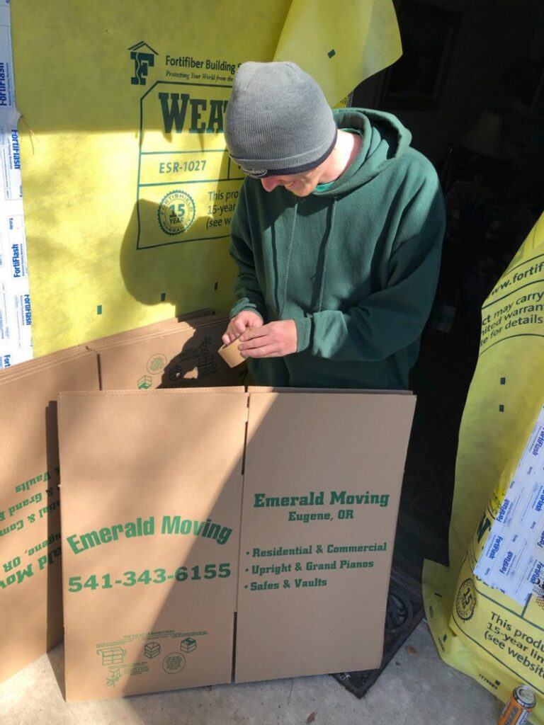A mover from Emerald Moving & Storage, Inc. taping a moving box with the company logo in Eugene, OR.