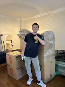 A Prime Moving professional giving a thumbs up next to packed boxes and wrapped furniture in Boston, MA.