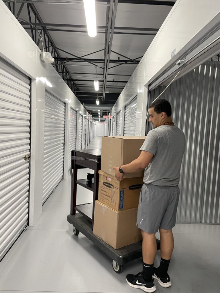 A Shield Moving Services mover transporting moving boxes on a cart through a storage facility hallway in Milwaukee, WI.