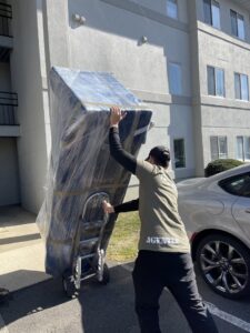 A mover from J.Gentle Van Lines transports a large, wrapped piece of furniture on a dolly outside an apartment building in Elizabeth, NJ.