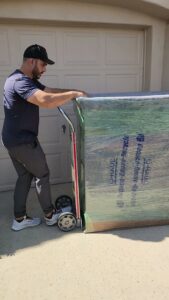 A professional mover transporting a large, wrapped piece of furniture on a hand truck for Az Student Movers in Scottsdale, AZ