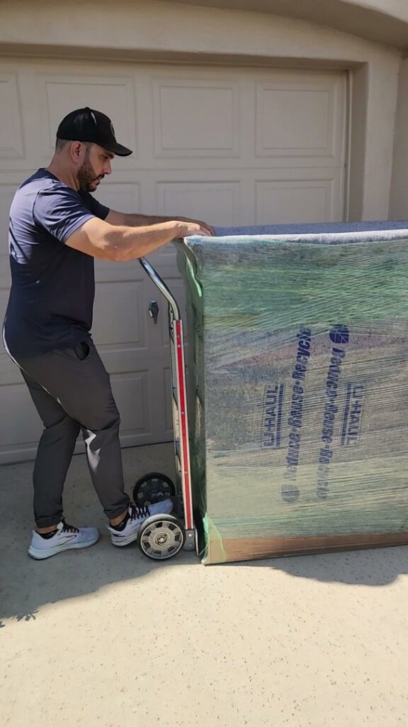 A professional mover transporting a large, wrapped piece of furniture on a hand truck for Az Student Movers in Scottsdale, AZ