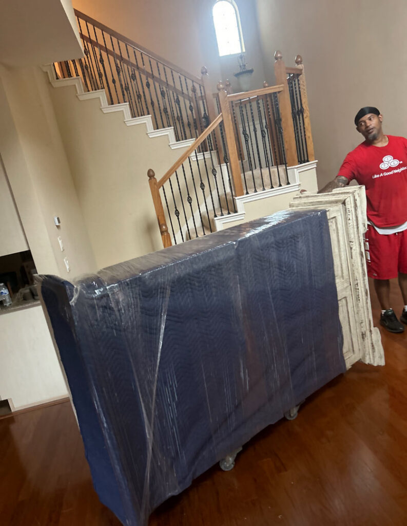 An Advantage Express Movers team member transporting a large, wrapped item on a dolly inside a home in Arlington, TX.