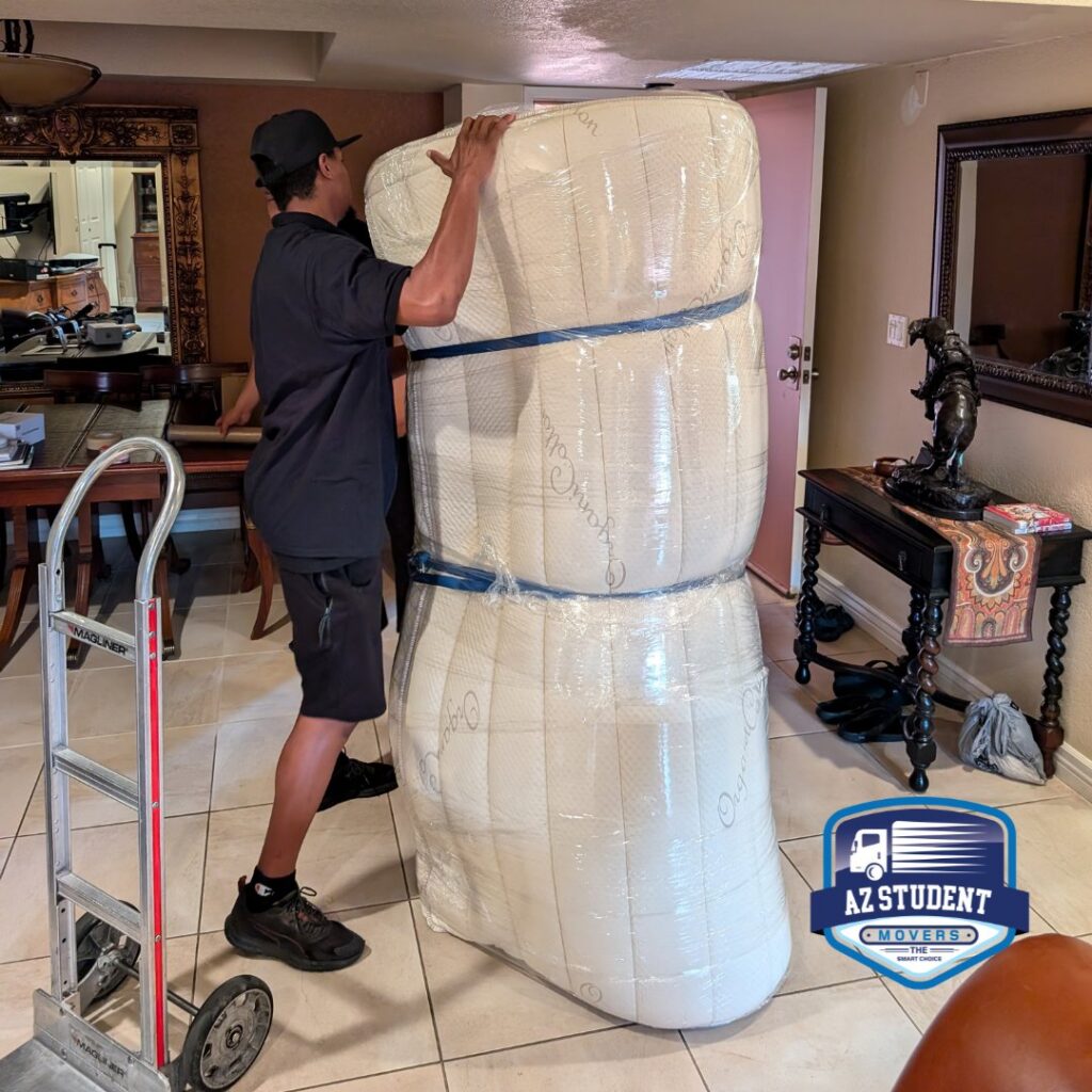 A professional mover transporting a stack of wrapped mattresses on a hand truck for Az Student Movers in Scottsdale, AZ