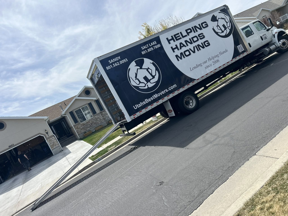A Helping Hands Moving & Maids truck with an extended ramp at a residential home, indicating a moving job in Salt Lake City, UT.