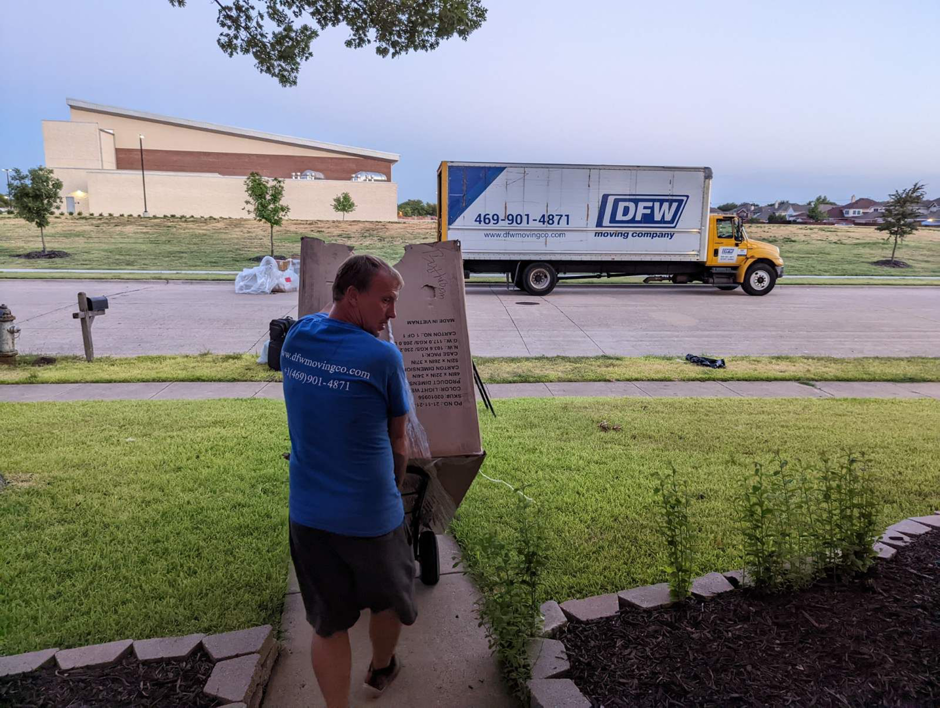 A mover from DFW Moving Company, LLC using a dolly to unload a box at a residence in Plano, TX.