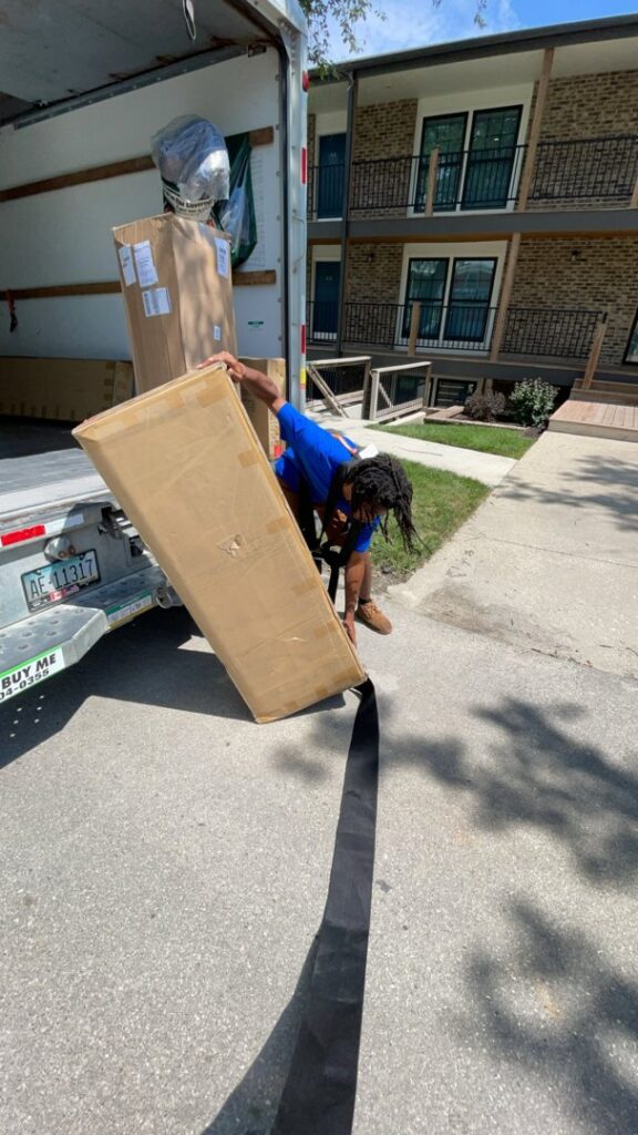An Ingenuity Moving professional carefully unloading a large box from a moving truck in Kansas City, MO.