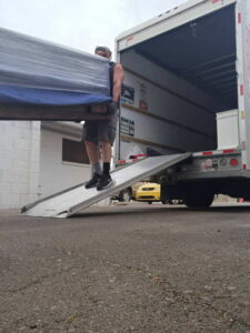 A professional mover unloading a large, wrapped piece of furniture down a ramp from a moving truck for Az Student Movers in Scottsdale, AZ