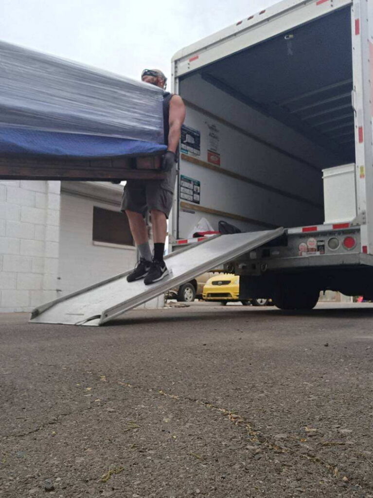 A professional mover unloading a large, wrapped piece of furniture down a ramp from a moving truck for Az Student Movers in Scottsdale, AZ