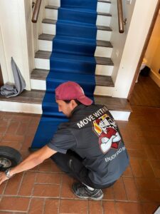 A mover unrolling a blue floor protector on a staircase, preparing for a move with All Way Moving in Washington, PA.