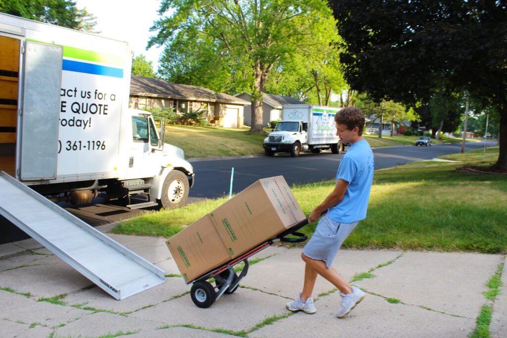 A mover using a hand truck to move a large box towards a moving truck ramp for Goal Line Moving in Maple Grove, MN.