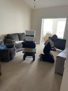 A mover with stacked boxes and luggage on a hand truck in a living room during a move by CNZ Moving in Raleigh, NC.