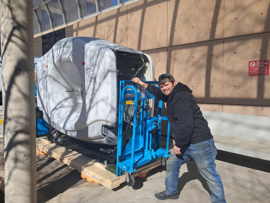 A mover standing next to large medical equipment being transported outside a facility by Peroulas Moving and Storage in Knoxville, TN