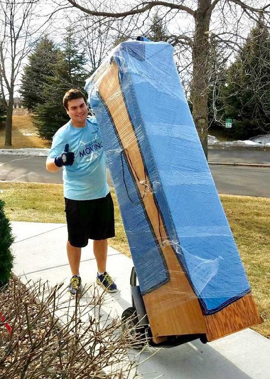 A mover giving a thumbs up next to a large, wrapped piece of furniture on a dolly for Goal Line Moving in Maple Grove, MN.