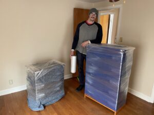 A Shield Moving Services mover standing with wrapped items and a roll of stretch wrap in Milwaukee, WI.