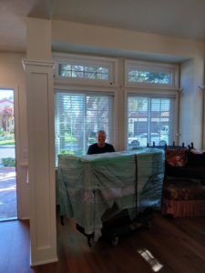 A mover with a carefully wrapped piano on a dolly inside a home by Rough Çutt Movers in San Diego, CA