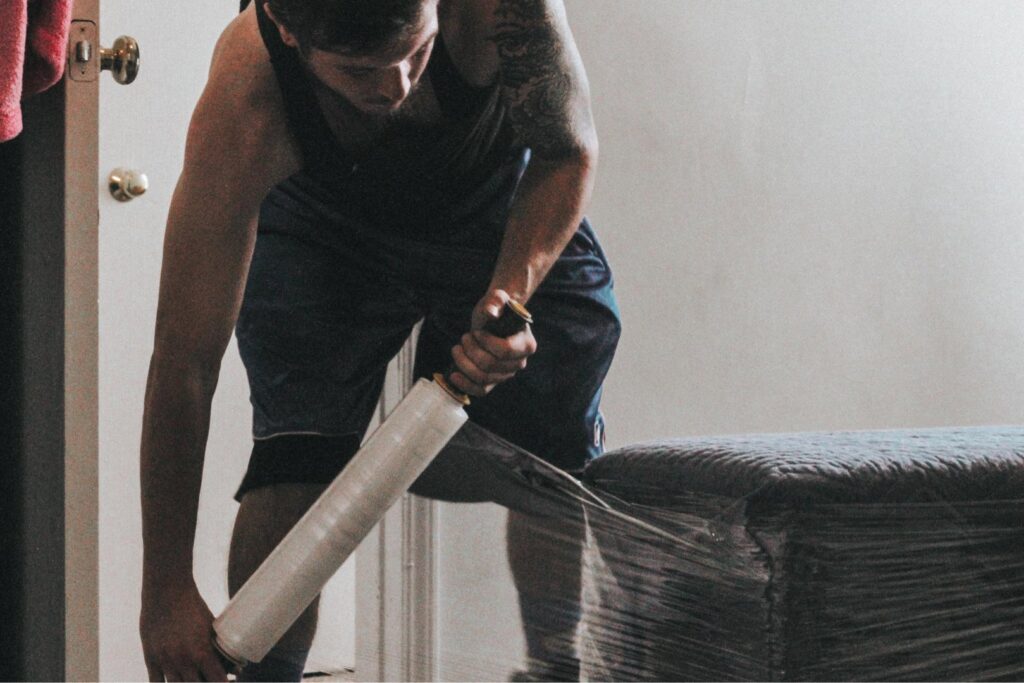 A professional mover from Ingenuity Moving carefully wrapping furniture with plastic film in Kansas City, MO.
