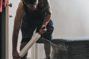 A professional mover from Ingenuity Moving carefully wrapping furniture with plastic film in Kansas City, MO.