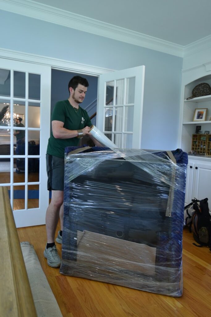 A Mastodon Moving LLC mover carefully wrapping a large piece of furniture with plastic and blankets in Westborough, MA.