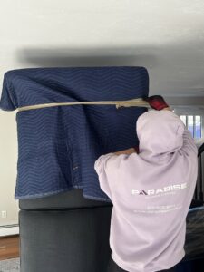 A mover from Paradise Moving & Storage wrapping furniture with a moving blanket and tape in Boston, MA.