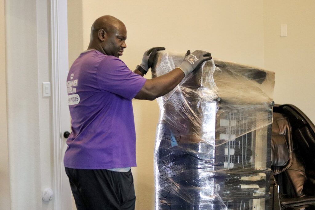 A professional mover from Kingdom Men Movers in Houston, TX, carefully wrapping a piece of furniture with plastic for protection.