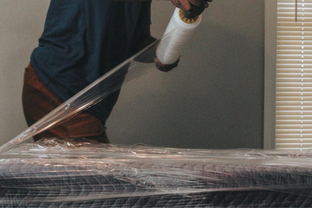 A professional mover from Ingenuity Moving wrapping a mattress with protective plastic in Kansas City, MO.