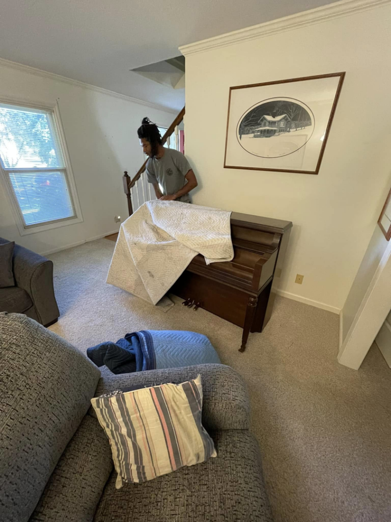 A mover from Ingenuity Moving wrapping a piano with a protective blanket in a home in Kansas City, MO.