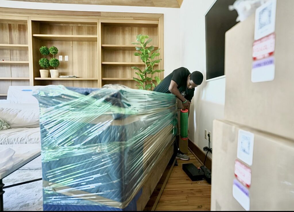 A professional mover from Gifted Journey Movers carefully wrapping a sofa with plastic for transport in Gulfport, MS.