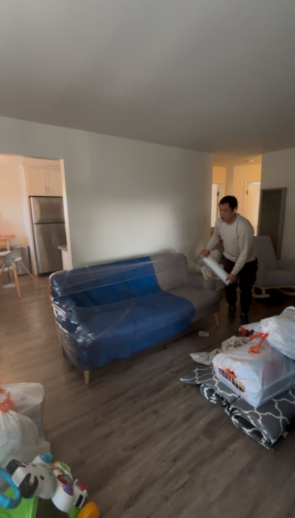 A mover wrapping a sofa with plastic inside a home for IMoving Professional Moving System Inc. in San Francisco, CA