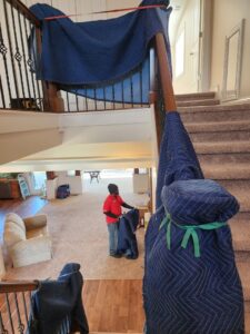 A professional mover from Joy Haul Professional Movers wrapping a staircase railing with a protective blanket in Columbia City, IN.