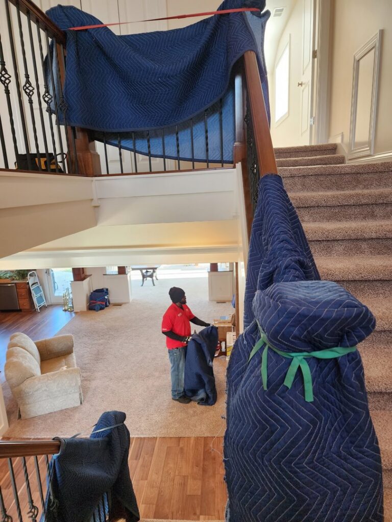 A professional mover from Joy Haul Professional Movers wrapping a staircase railing with a protective blanket in Columbia City, IN.