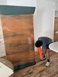 A professional mover from Gifted Journey Movers wrapping a tall piece of furniture with plastic for protection in Gulfport, MS.