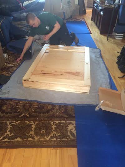 A Mastodon Moving LLC mover kneeling and wrapping a wooden item on a protective mat in Westborough, MA.