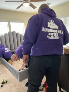Two professional movers from Kingdom Men Movers in Houston, TX, assembling a bed frame in a bedroom.