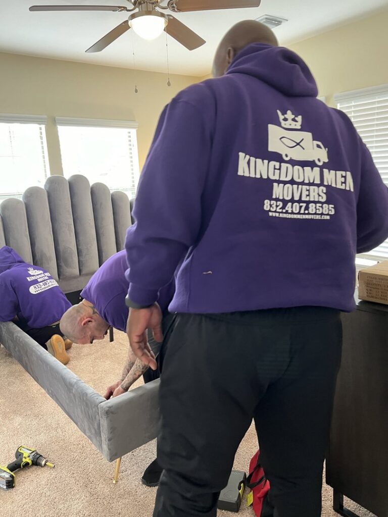 Two professional movers from Kingdom Men Movers in Houston, TX, assembling a bed frame in a bedroom.