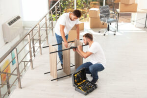 Two movers from Three Movers in Henderson, NV, assembling a piece of furniture with tools.
