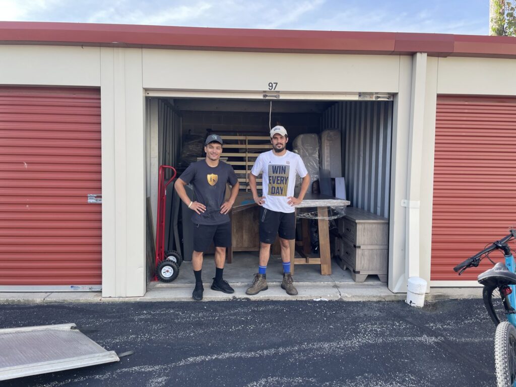 Two Shield Moving Services movers standing in front of an open storage unit filled with furniture in Milwaukee, WI.