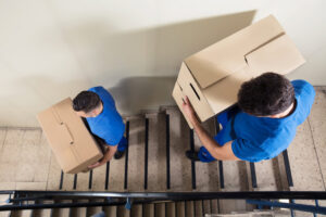An overhead view of two professional movers from Three Movers in Henderson, NV, carrying cardboard boxes down a staircase.