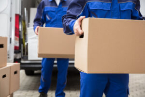 Two professional movers from Three Movers in Henderson, NV, carrying cardboard boxes towards a moving van.