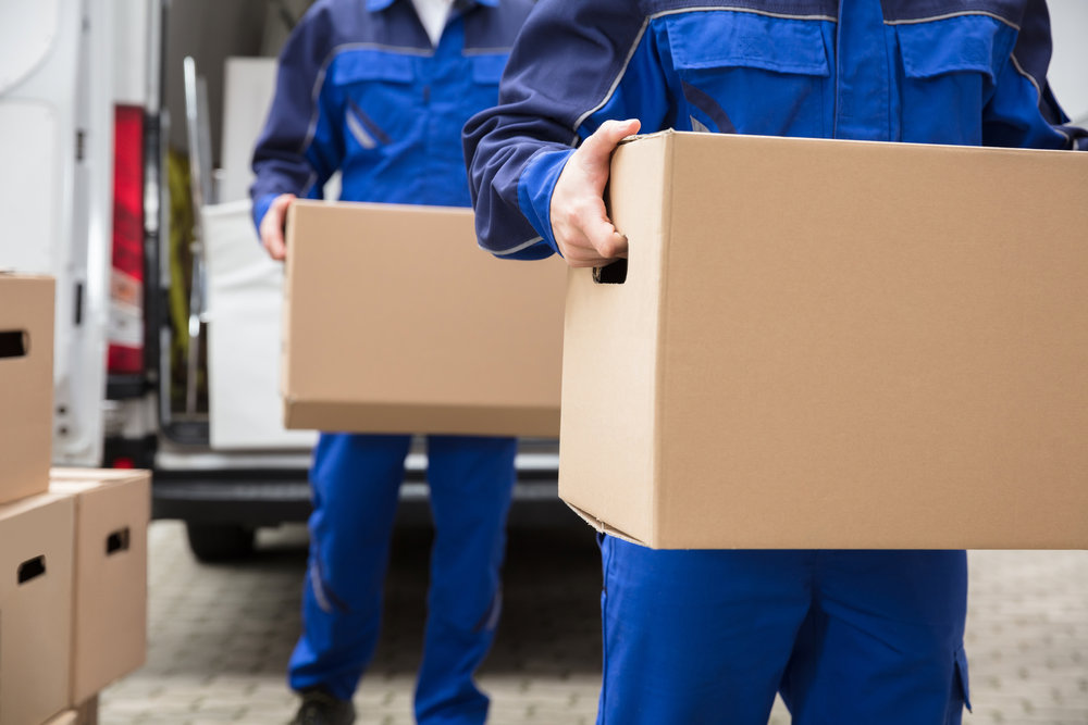 Two professional movers from Three Movers in Henderson, NV, carrying cardboard boxes towards a moving van.