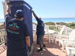 Two movers from Cheap Movers Los Angeles carrying blanket-wrapped furniture on a balcony with an ocean view in Los Angeles, CA.