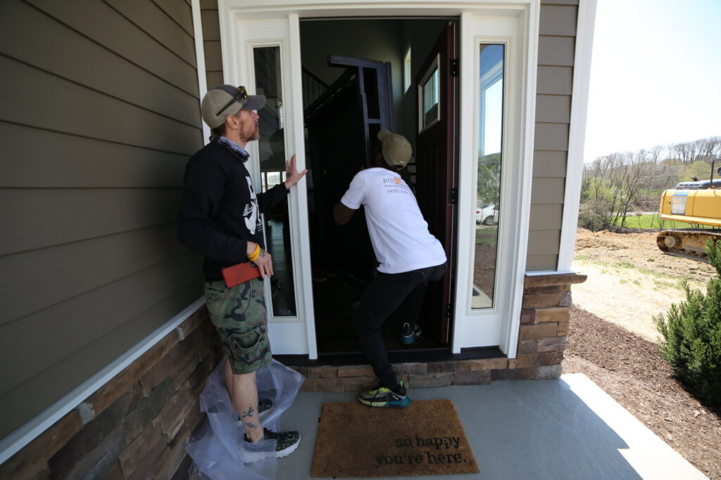 Two PittMovers team members carefully carrying a piece of furniture through the front door of a house in McKees Rocks, PA