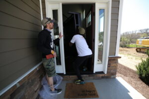 Two PittMovers team members carefully carrying a piece of furniture through the front door of a house in McKees Rocks, PA