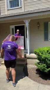Two movers from Paradise Moving & Storage carrying a wrapped item out of a house in Boston, MA.