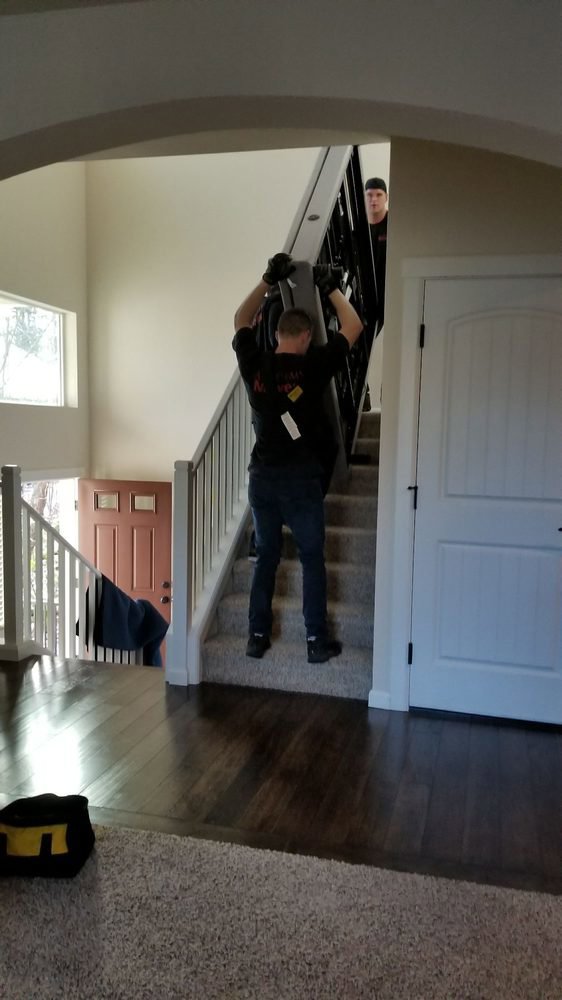 Two Academy Movers team members carefully carrying a large, flat item up a staircase inside a home in Gilbert, AZ.